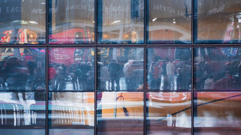 Multiple panes of glass windows layered with reflections of an indoor crowd and architectural elements.
