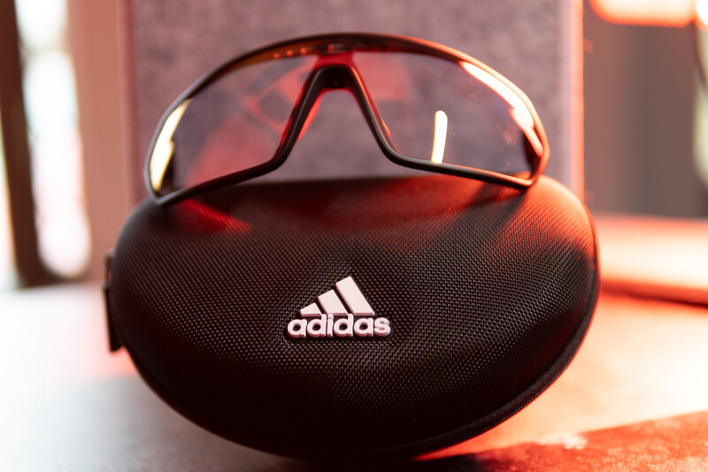 Adidas sports sunglasses in a black protective case with warm golden hour lighting.