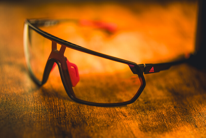 Red-framed sports glasses resting on warm golden-orange textured surface with blurred background.
