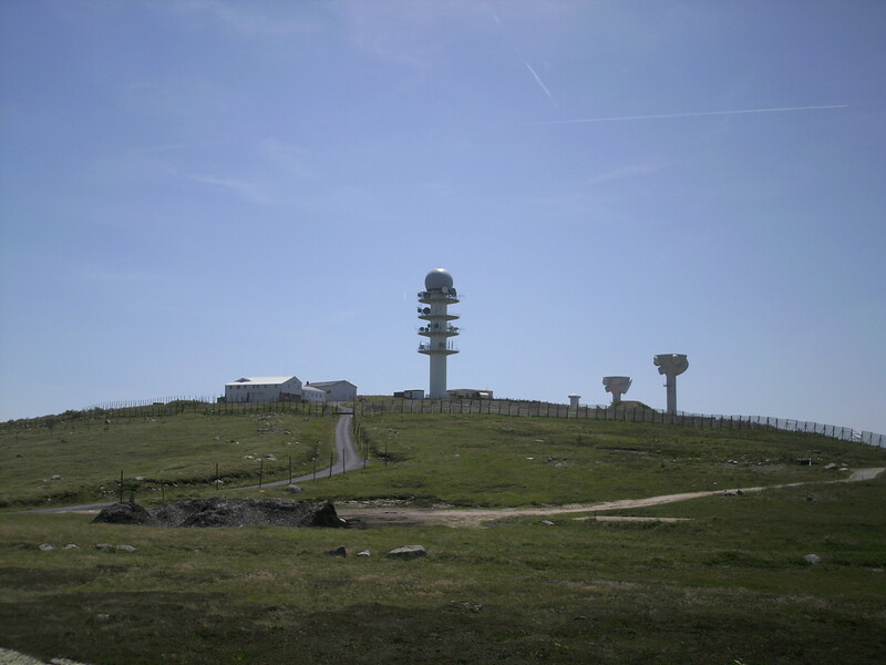 Hilltop landscape with communication towers and green grassland under clear blue sky.
