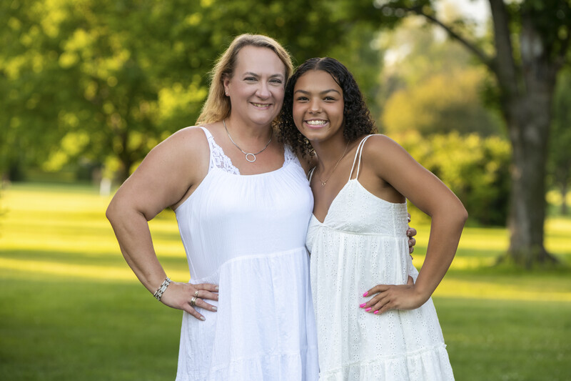 Two women in white dresses posing together outdoors with hands on hips.