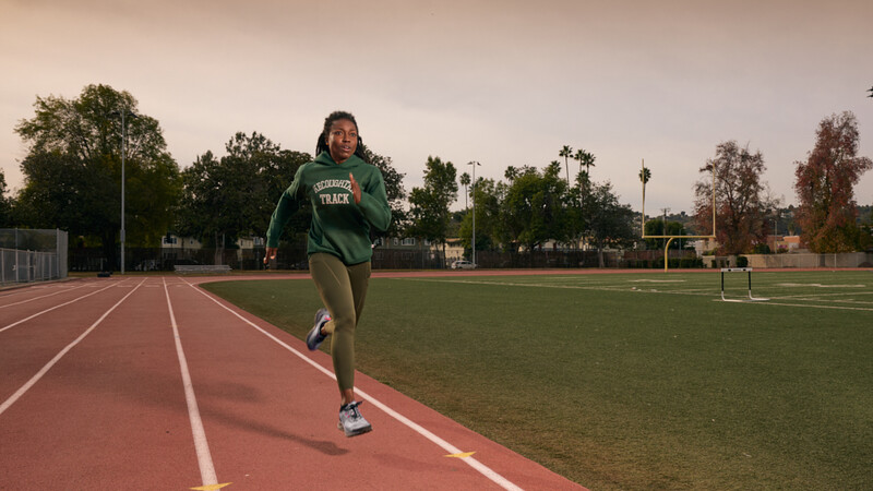 Athlete running on a red track at an outdoor sports facility during golden hour.