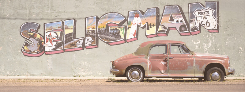 Rusty vintage car parked against a weathered wall mural reading 'SELIGMAN' with Route 66 imagery.