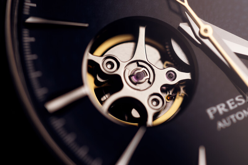 Close-up of an automatic watch movement and dial showing the open caseback with visible gears and escapement wheel.
