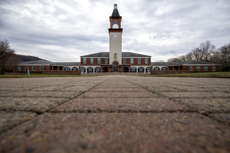 Red brick institutional building with central clock tower, photographed from ground level along a paved plaza.