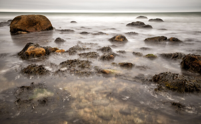Rocky coastal shoreline with boulders partially submerged in misty seawater.