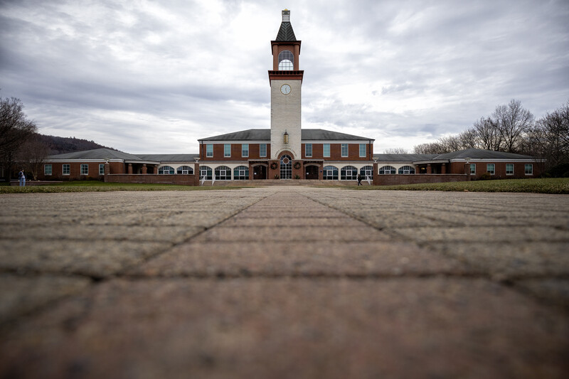 Red brick building with white clock tower viewed from ground level across empty courtyard.