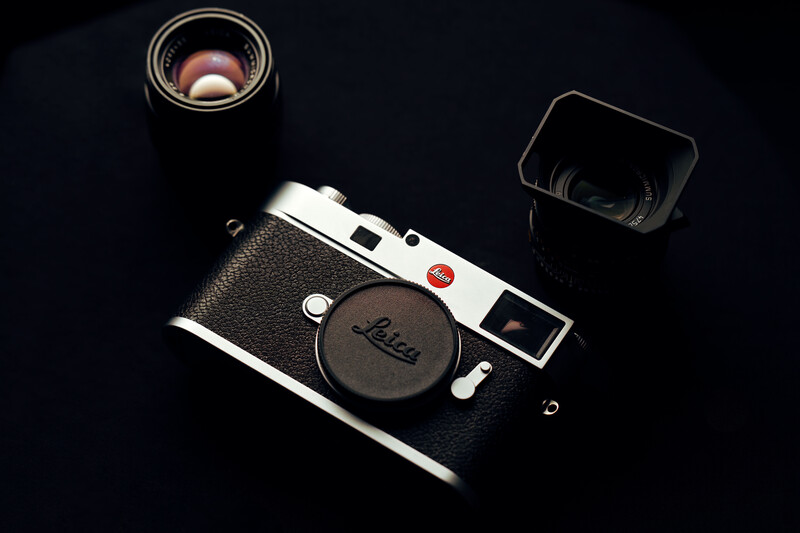 Leica M rangefinder camera with chrome and black leather body, displayed with three lenses on dark background.