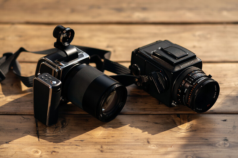 Two vintage medium format film cameras positioned on wooden surface with natural sunlight.