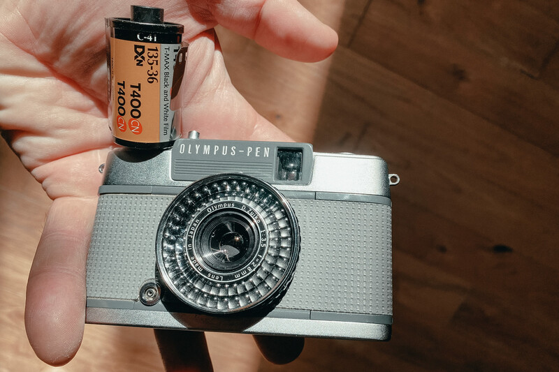 Hand holding an Olympus PEN EE2 with a roll of Kodak T400 CN film