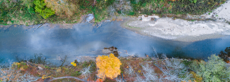 Aerial view of a river bend with autumn foliage and bare trees along both banks.