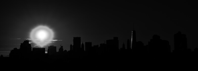 Silhouetted city skyline against a bright moon rising behind low clouds at dusk or night.