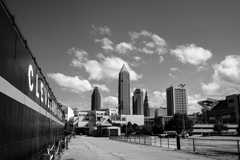 Black and white cityscape showing downtown skyline with art deco buildings and modern skyscrapers under partly cloudy sky.