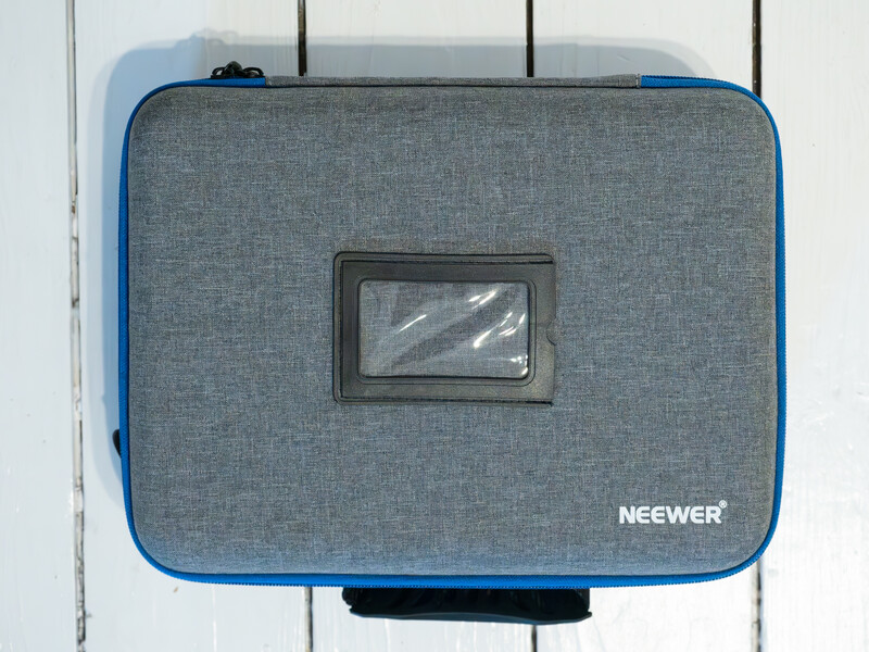 Neewer camera equipment case with gray fabric exterior and blue trim on white wooden surface.