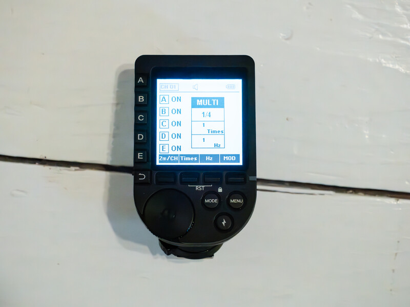Remote control with small LCD screen displaying menu options mounted on white wall.