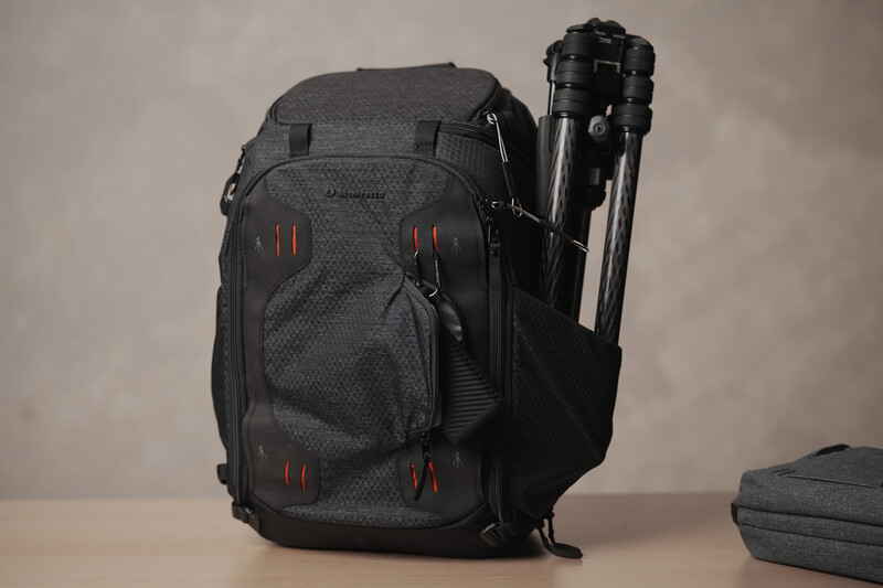 Dark gray camera backpack with tripod holder and red accent stitching displayed against neutral background.