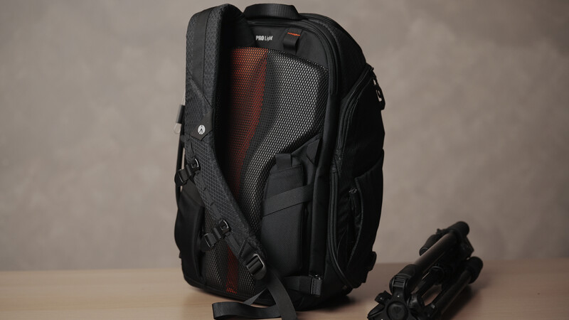 Black photography backpack displayed open, showing red mesh interior padding and organizational compartments.
