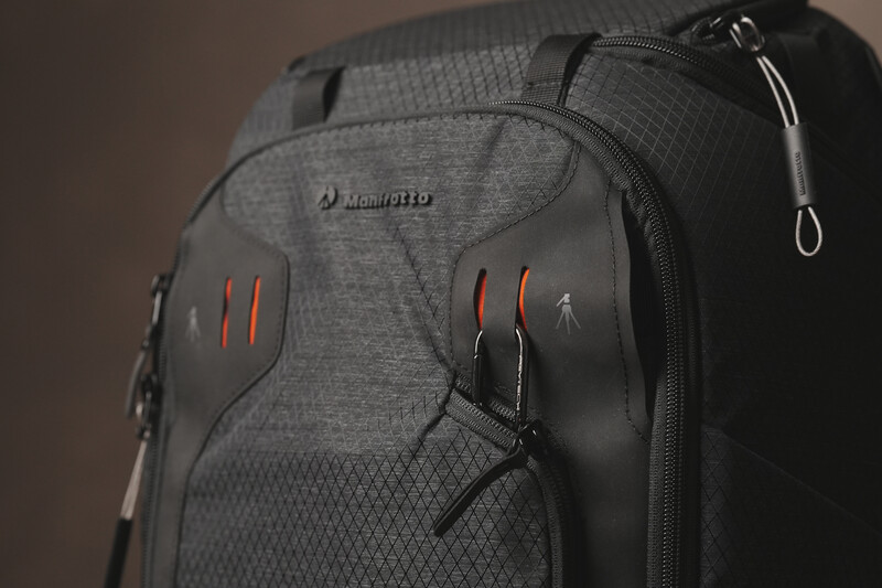 Gray camera backpack with red accent straps and multiple zippered compartments against a neutral brown background.