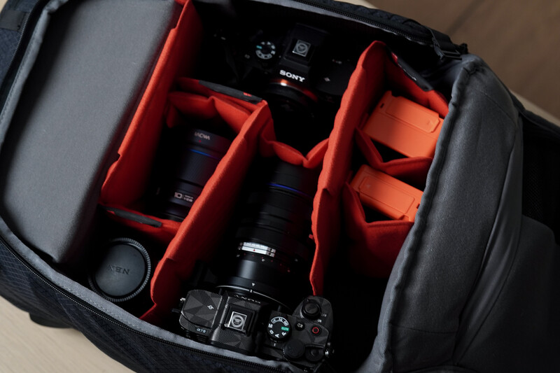 Sony camera with lenses and accessories organized in red foam compartments inside a black camera bag.