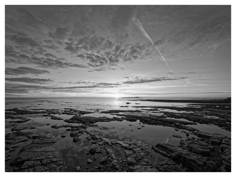 Tidal mudflats with shallow pools under a dramatic cloudy sky at low tide.