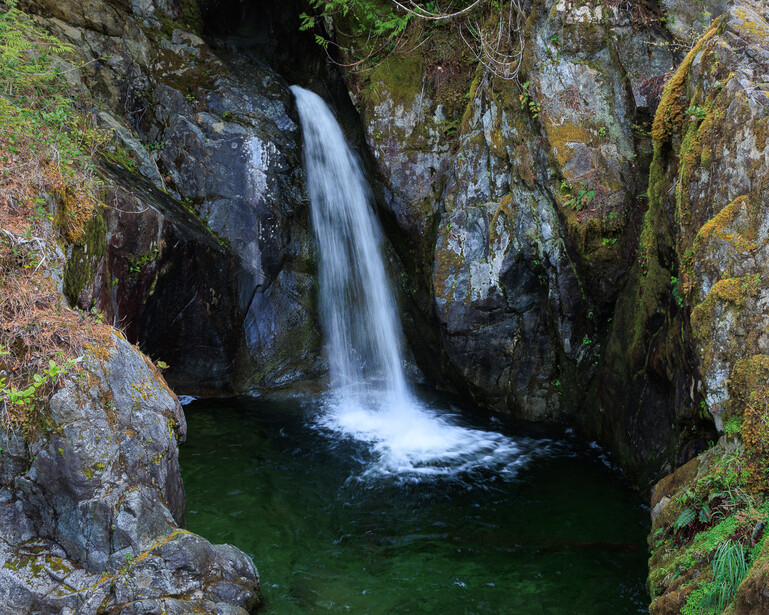 A waterfall falls into a calm pool surrounded by rocks