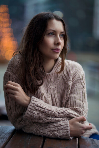Woman in beige knit sweater looking to the side, shot outdoors during golden hour.
