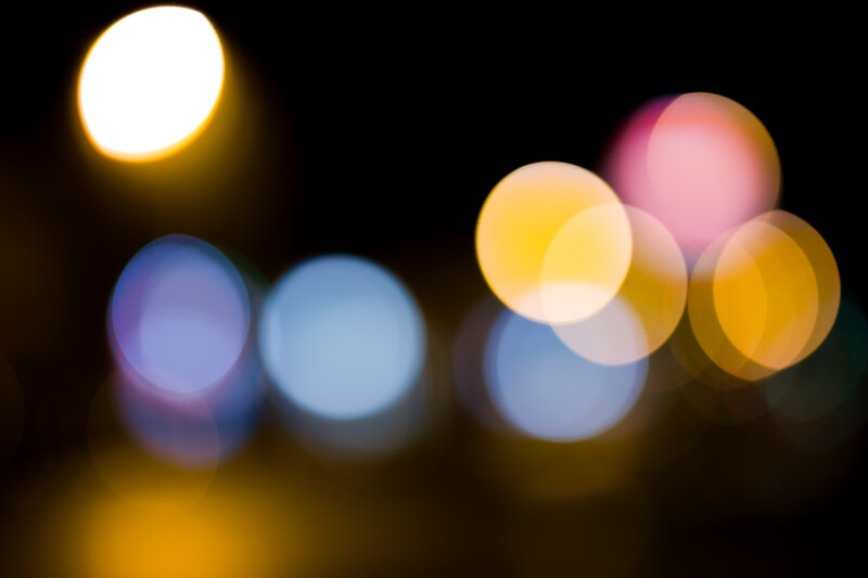 Bokeh lights in blue, yellow, pink, and warm tones blurred against a dark background.
