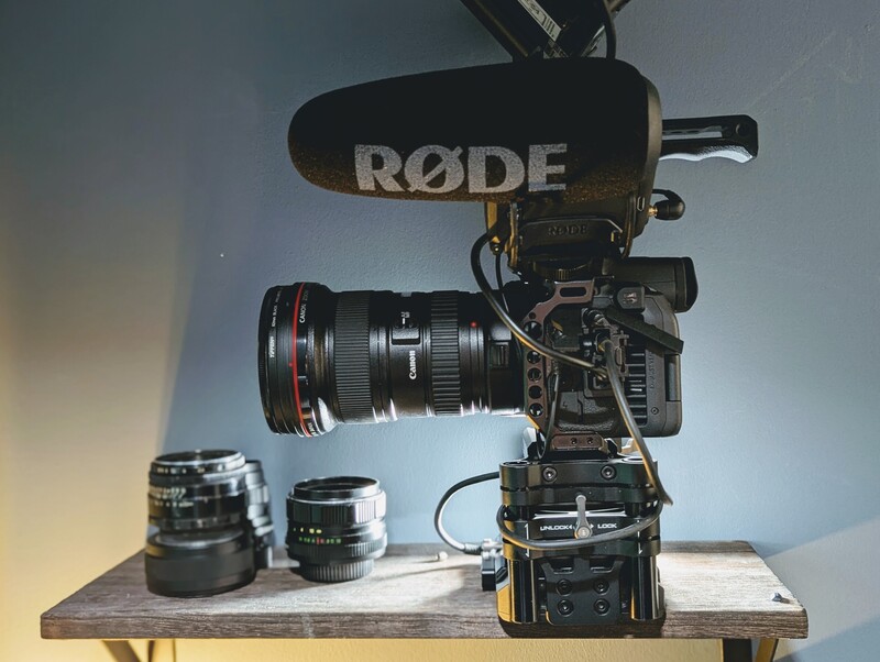 Professional cinema camera setup with RODE microphone, cinema lens, and support equipment on wooden bench.