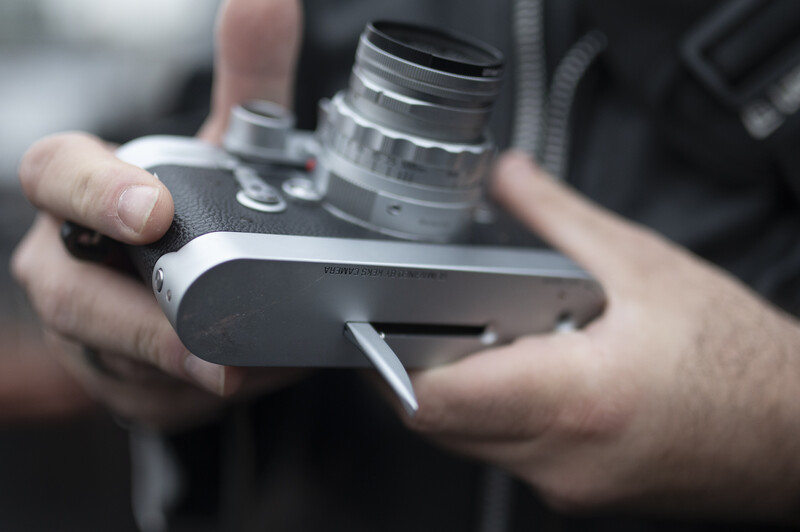 Photographer's hands holding a mirrorless camera with mounted lens in outdoor setting.