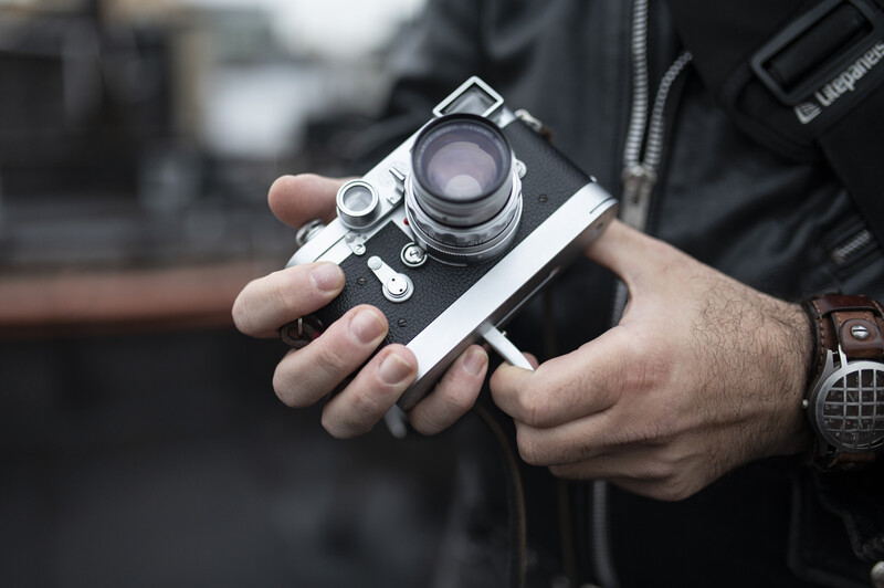 Photographer's hands holding a vintage rangefinder camera with chrome body and glass lens element.