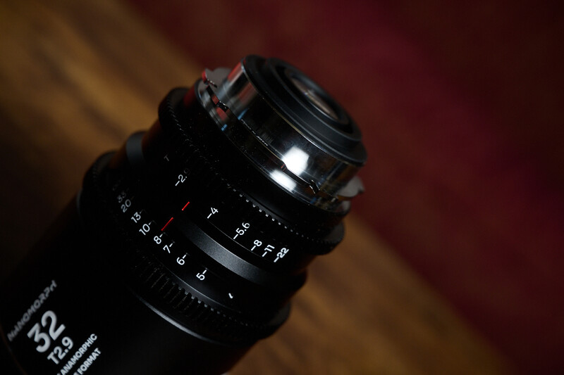 Close-up of a vintage manual focus lens with distance scale and aperture markings visible against a warm, blurred background.