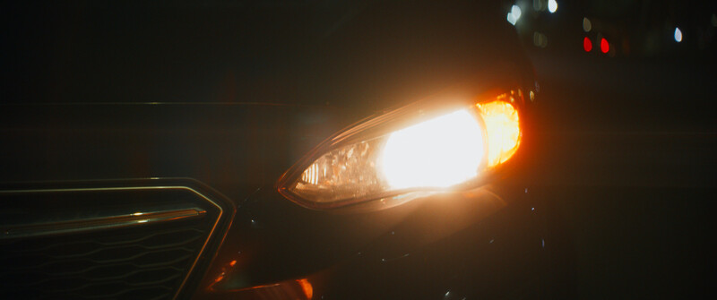 Close-up of a vehicle's headlight glowing brightly against a dark background at night.