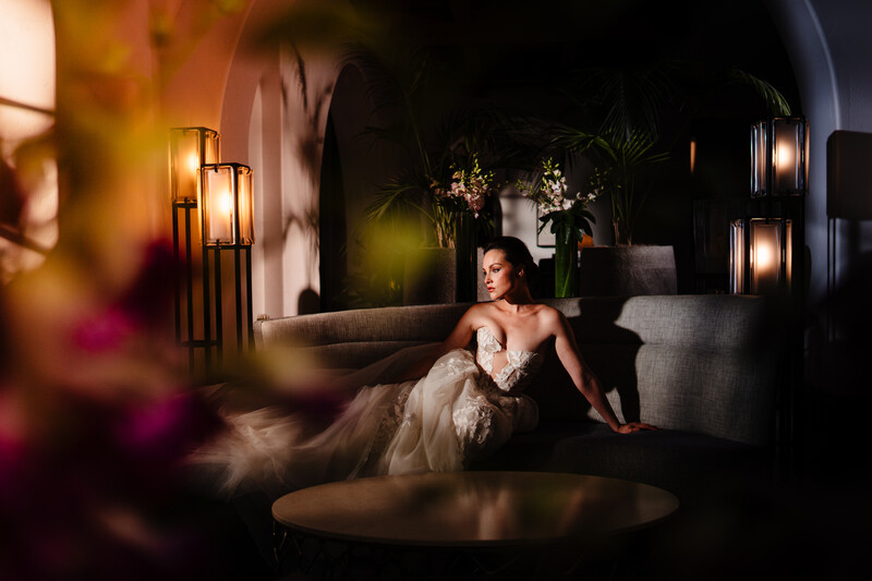 Bride in tulle gown seated in dark architectural space lit by warm pendant lights.