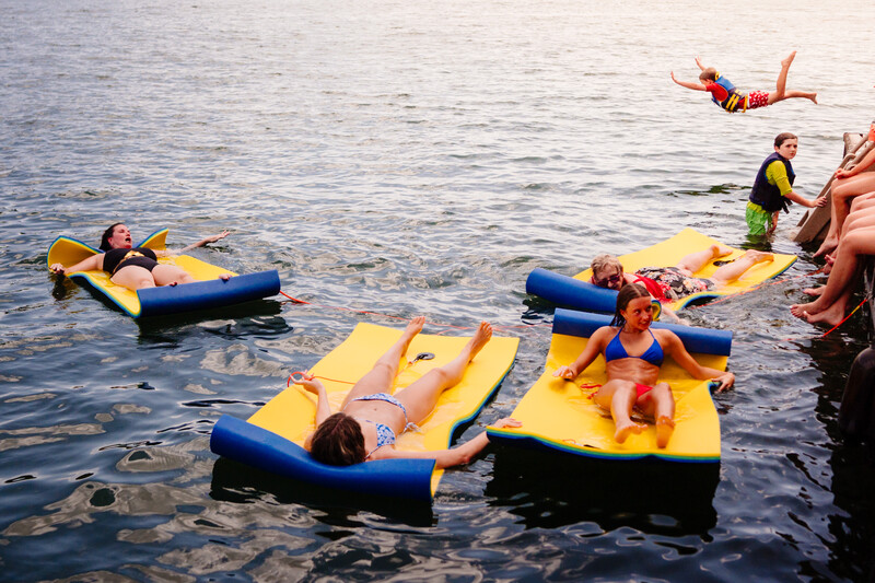 Group of people floating on yellow and blue inflatable water platforms in shallow water during daytime.