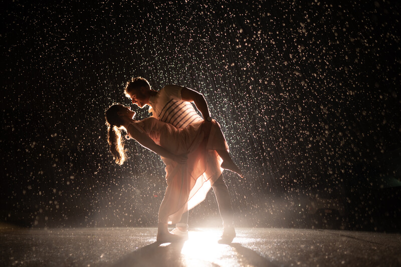 Male athlete in dynamic motion under dramatic overhead lighting with heavy rain or water spray effect.