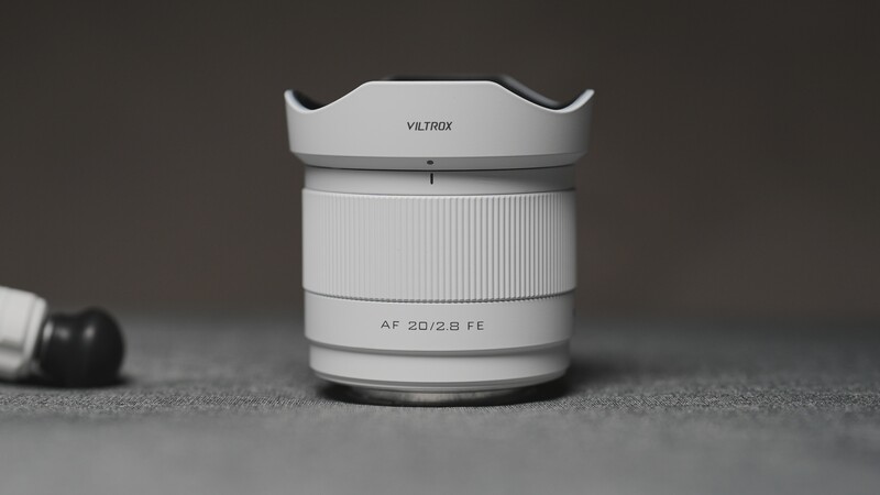 Viltrox AF 20/2.8 FE lens with hood on gray surface next to lens cap.