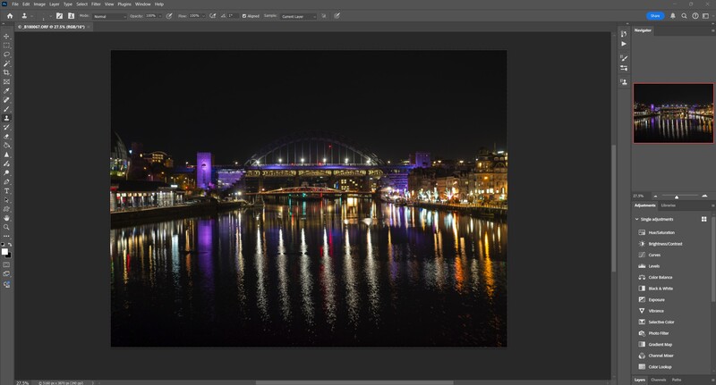 Night cityscape with illuminated buildings and bridges reflected in calm water.