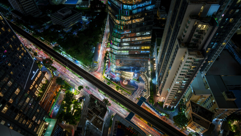 Overhead view of illuminated urban street at night with traffic, buildings, and neon signage.