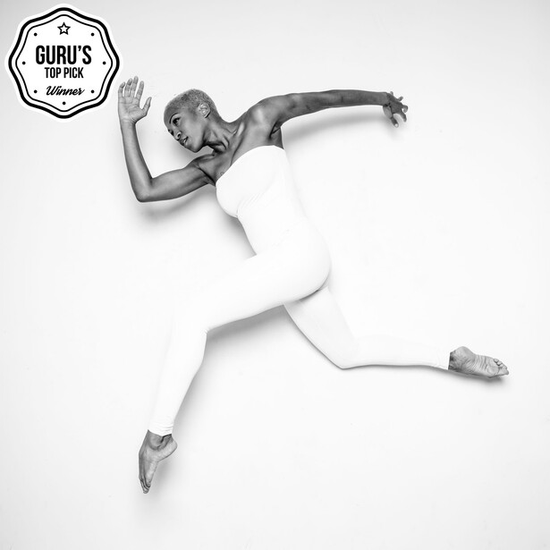 Overhead black and white photograph of a ballet dancer in mid-leap against a white background.