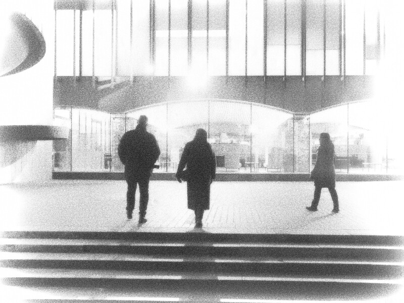 Three silhouetted figures standing in a modern interior with large windows and overhead architectural elements.