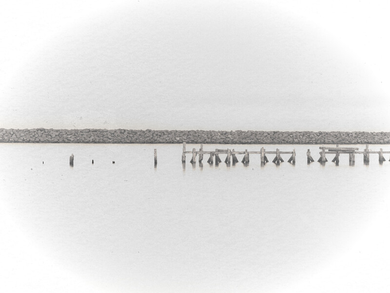Minimalist black and white landscape with wooden posts extending into still water beneath an overcast sky.