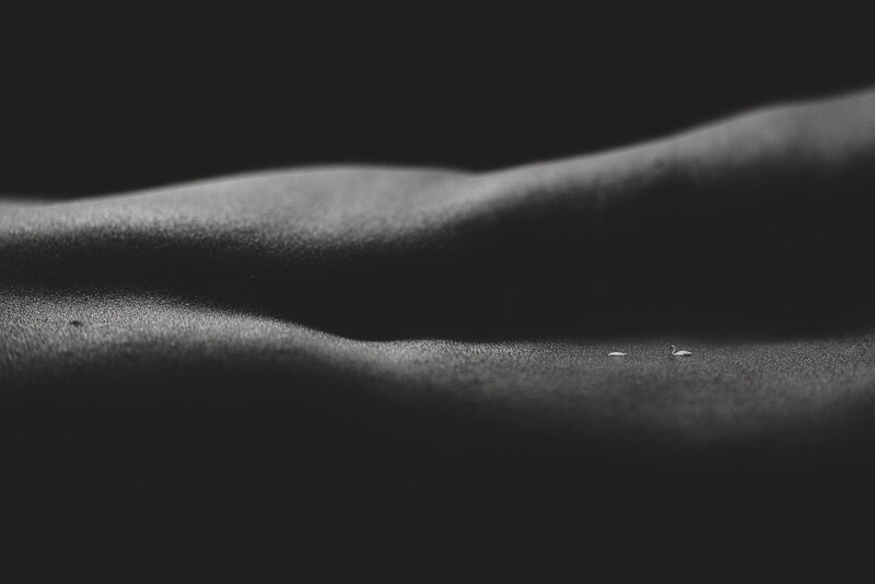 Close-up of human skin showing texture and contours lit by dramatic side lighting against a dark background.