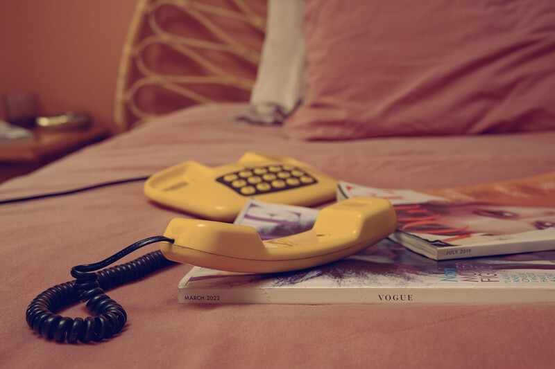 Vintage yellow rotary telephone with coiled cord resting on a bed next to magazine pages.