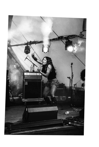 Musician performing on stage with guitar and amplifier, shot from below against dramatic overhead lighting.