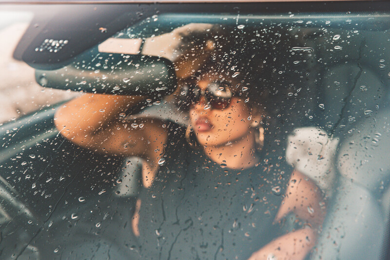 Two people visible through a rain-covered car window, their faces partially obscured by water droplets.