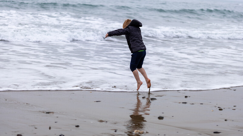 Person mid-jump on wet beach sand with ocean waves in background.