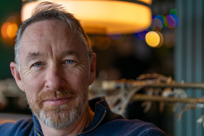 Male portrait with natural warm and cool ambient lighting in an interior setting.