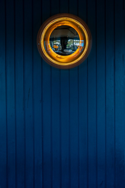 Golden circular porthole window set into a vertical blue corrugated metal wall.