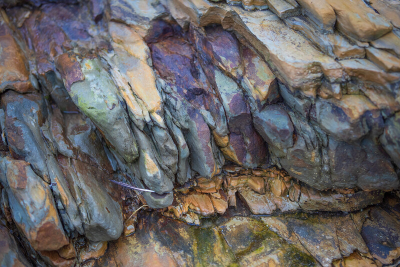 Closeup of layered slate rock formations with natural purple, blue, and rust-colored mineral striations.