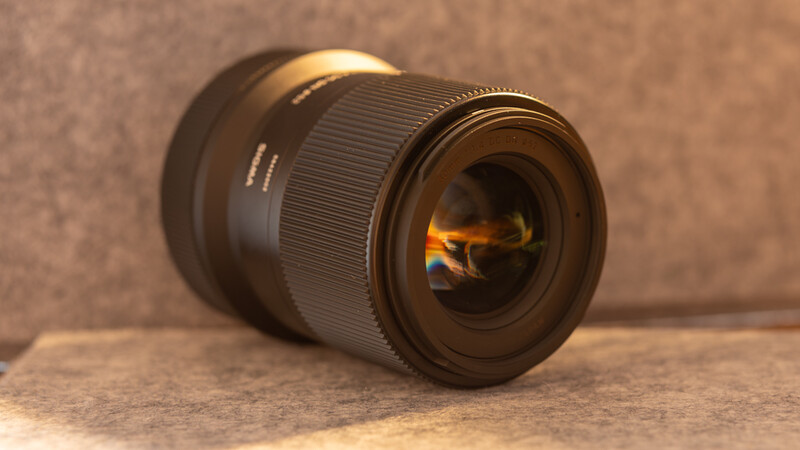 Black telephoto lens positioned horizontally on tan surface with warm backlighting illuminating the front element.